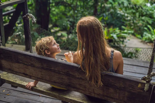 Anne ve oğlu gündüz tropikal bahçe salıncak üzerinde oturan