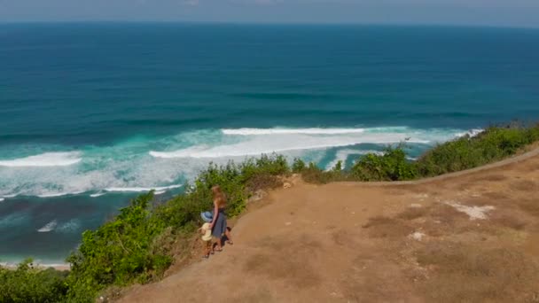 空中拍摄的一个年轻女子和她的儿子访问一个偏远的海滩-nyang nyang-在巴厘岛上。站在岩石上看着他们面前的开阔的大海. — 图库视频影像