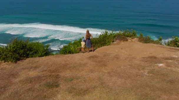 Zdjęcia lotnicze z młodą kobietę i jej syn, odwiedzając zdalnego beach - nyang nyang - na wyspie Bali. Stojąc na skale patrząc na otwartym oceanie przed nimi. — Wideo stockowe