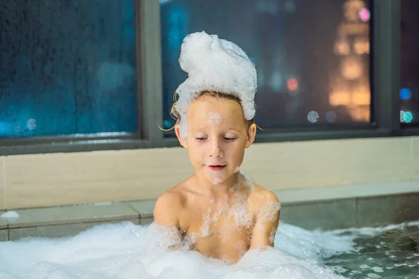快乐的小男孩坐在浴缸里 晚上睡觉前 窗户俯瞰城市的背景 沐浴在窗前满是泡沫的婴儿的肖像 — 图库照片