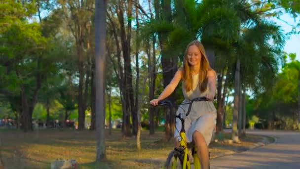 Steadycam shot of a young woman riding a bicycle in a tropical park — Stock Video