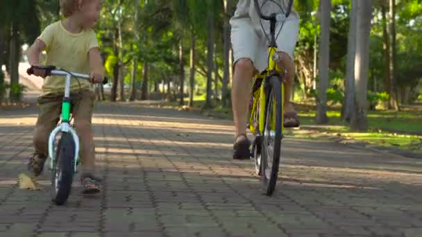 Steadycam tiro de uma jovem mulher e seu filho montando uma bicicleta e runbike em um parque tropical — Vídeo de Stock