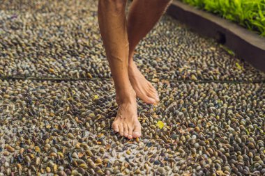 Man Walking On A Textured Cobble Pavement, Reflexology. Pebble stones on the pavement for foot reflexology. clipart