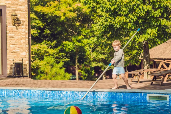 Yürümeye başlayan çocuk havuzunu temizliyor ve topu havuzdan çeker. Havuz temizleyicisi kavramı.