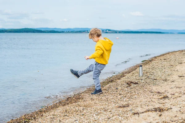 Young boy throwing stones in sea water from beach at daytime