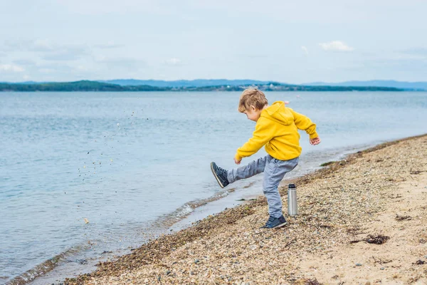 Young boy throwing stones in sea water from beach at daytime