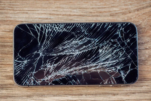 Smartphone display with broken glass on a wooden table