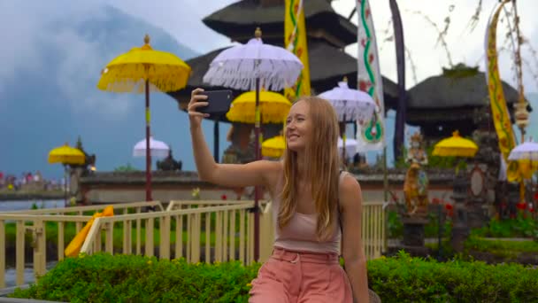 Langsamaufnahme einer jungen Frau, die ein Selfie macht, vor einem Pura Ulun Danu Tempel am Bratan-See in Bali, Indonesien — Stockvideo