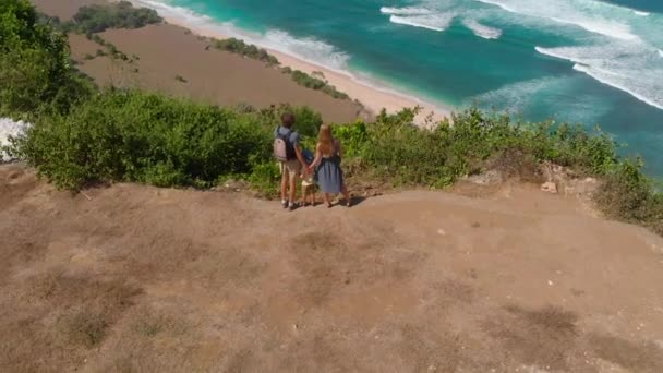 Slowmotion κεραία βολή της μια ευτυχισμένη οικογένεια που επισκέπτονται μια απομακρυσμένη παραλία - nyang nyang-σχετικά με το νησί του Μπαλί. Στέκεται πάνω σε ένα βράχο που βλέπουν σε μια ανοικτή ωκεανό μπροστά τους — Αρχείο Βίντεο