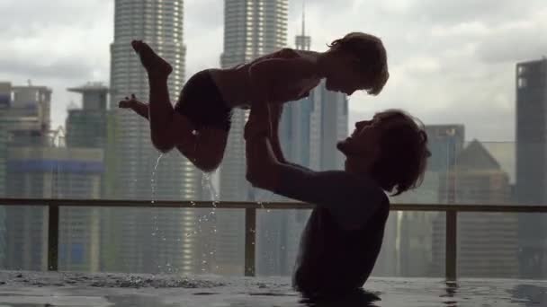 Kuala Lumpur, Malezja-12 maja 2018: Ojciec i syn, zabawy w basenie na dachu z widokiem na wieżowce — Wideo stockowe
