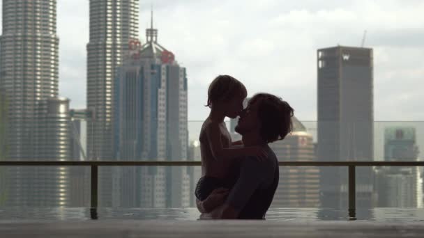 Kuala-Lumpur, Maleisië-12 mei 2018: Vader en zoon met plezier in een zwembad op het dak met uitzicht op de wolkenkrabbers — Stockvideo