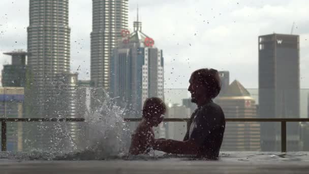 Kuala-Lumpur, Maleisië-12 mei 2018: Vader en zoon met plezier in een zwembad op het dak met uitzicht op de wolkenkrabbers — Stockvideo