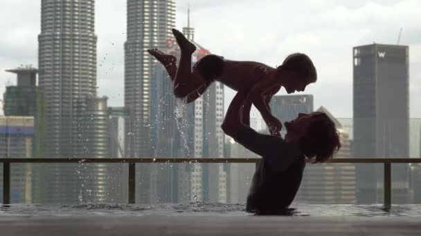 Kuala-Lumpur, Malásia - 12 de maio de 2018: Pai e filho se divertindo em uma piscina no terraço com vista para os arranha-céus — Vídeo de Stock