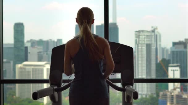 Ung kvinna i ett gym på toppen av en skyskrapa utbildning på en löparbana med utsikt över en hel stad — Stockvideo
