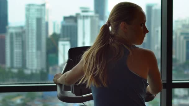 Kuala-Lumpur, Maleisië-12 mei 2018: Jonge vrouw in een sportschool op de top van een wolkenkrabber-training op een hometrainer met een uitzicht op een hele stad — Stockvideo