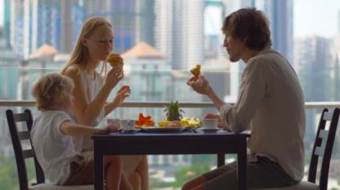 Genç aile bir kahvaltı, Bütün şehir şehir manzaralı bir gökdelen onların balkonda yemek