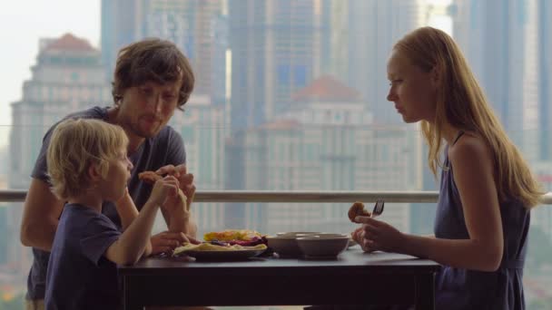 Familia joven desayunando, almorzando en su balcón en un rascacielos con vistas a todo el centro de la ciudad — Vídeos de Stock