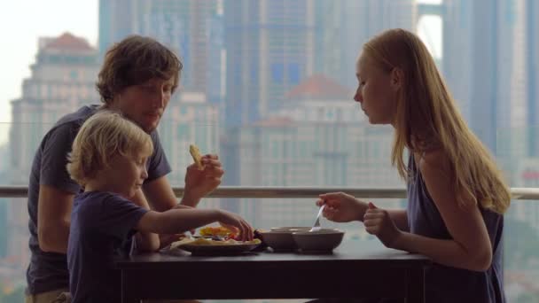 Молода сім'я снідає, обідає на балконі в хмарочосі з видом на все місто — стокове відео
