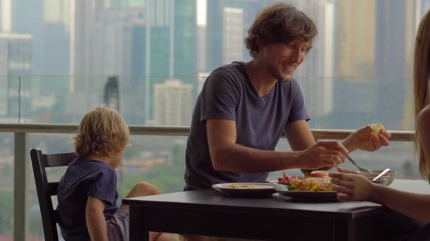 朝食を持っている若い家族、市全体のダウンタウンの景色を超高層ビルのバルコニーでランチ — ストック動画