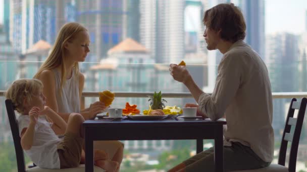 Νεαρή οικογένεια έχοντας ένα πρωινό, το μεσημεριανό γεύμα στο μπαλκόνι τους σε ένα ουρανοξύστη με θέα σε όλο το λεκανοπέδιο της πόλης — Αρχείο Βίντεο