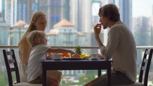 Giovane famiglia che fa colazione, pranzo sul balcone in un grattacielo con vista su un intero centro della città — Video Stock