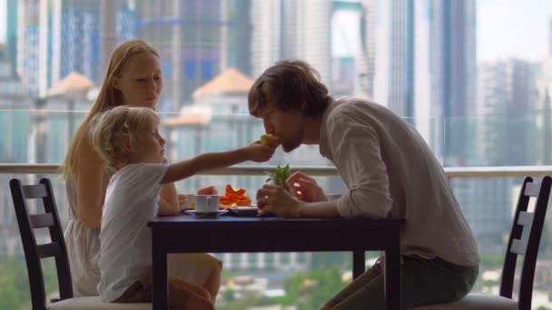 Jong gezin met een ontbijt, lunch op hun balkon in een wolkenkrabber met uitzicht op een hele centrum van de stad — Stockvideo