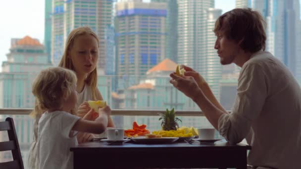 Jong gezin met een ontbijt, lunch op hun balkon in een wolkenkrabber met uitzicht op een hele centrum van de stad — Stockvideo