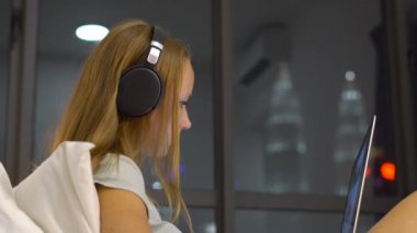 Genç kadın giyiyor kablosuz kulaklıklar üzerinde oturan bir dizüstü bilgisayar kullanarak çalışma ısıtmak bir amaç, siluetleri ile yatak