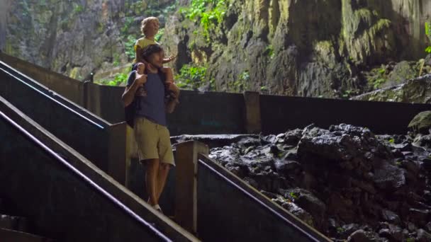 Father hanging his son on a shoulders walking up the stairs inside of an ancient Batu caves in Malaysia having a hindu temple inside — Stock Video