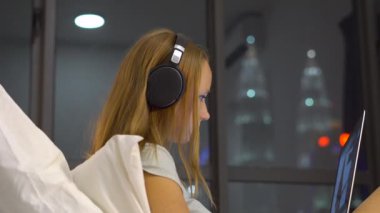 Genç kadın giyiyor kablosuz kulaklıklar üzerinde oturan bir dizüstü bilgisayar kullanarak çalışma ısıtmak bir amaç, siluetleri ile yatak