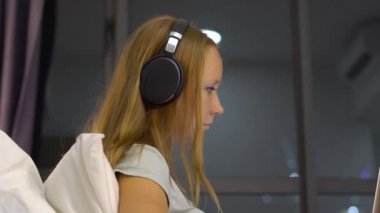 Genç kadın giyiyor kablosuz kulaklıklar üzerinde oturan bir dizüstü bilgisayar kullanarak çalışma ısıtmak bir amaç, siluetleri ile yatak