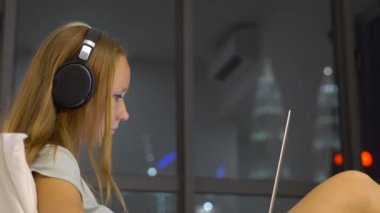 Genç kadın giyiyor kablosuz kulaklıklar üzerinde oturan bir dizüstü bilgisayar kullanarak çalışma ısıtmak bir amaç, siluetleri ile yatak