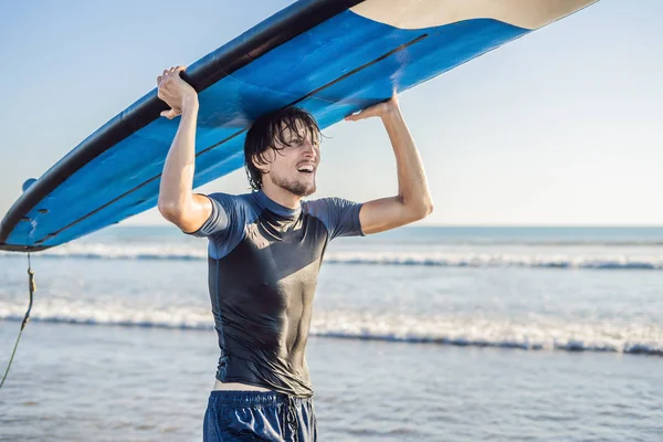 Man carrying surfboard over his head. Closeup of handsome guy with surfboard on head at beach. Portrait of man carrying surfboard on hid head and smiling at beach.