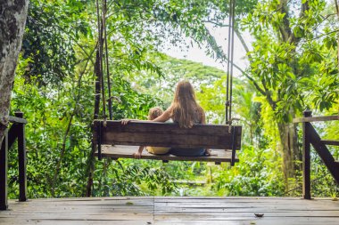 Anne ve oğlu gündüz tropikal bahçe salıncak üzerinde oturan