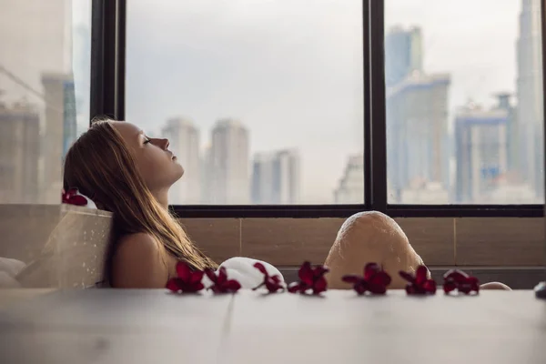 Молода Жінка Сидить Ванні Піною Квітами Франгіпані Тлі Панорамного Вікна — стокове фото