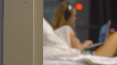 Genç kadın giyiyor kablosuz kulaklıklar üzerinde oturan bir dizüstü bilgisayar kullanarak çalışma ısıtmak bir amaç, siluetleri ile yatak
