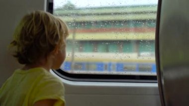 Küçük çocuk bir pencere içinde hareket eden bir trenin önünde oturan