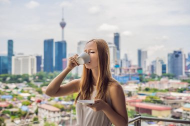 Genç kadın içecekler kahve sabah büyük şehir ve gökdelenler manzaralı balkon.