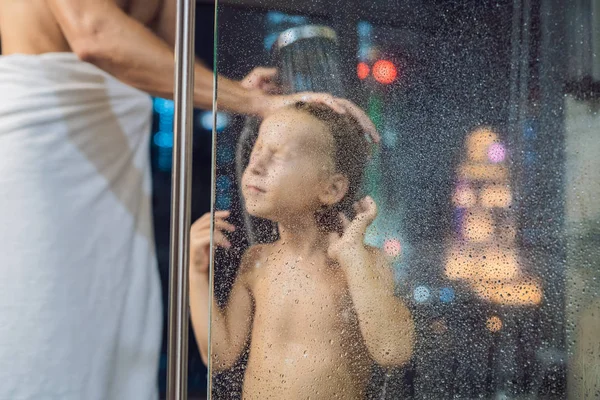 爸爸晚上在淋浴的时候洗他儿子的头发 然后睡在窗户的背景上 俯瞰着城市的全景 — 图库照片
