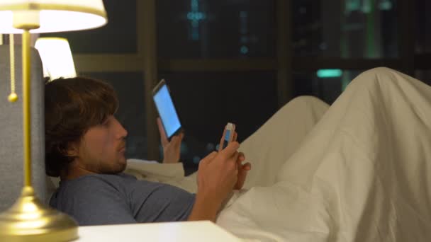Homme et femme couchés dans le lit chacun avec smartphone et tablette pc. problèmes dans le mariage et les relations intersexuelles problèmes et appareils mobiles concept de dépendance — Video