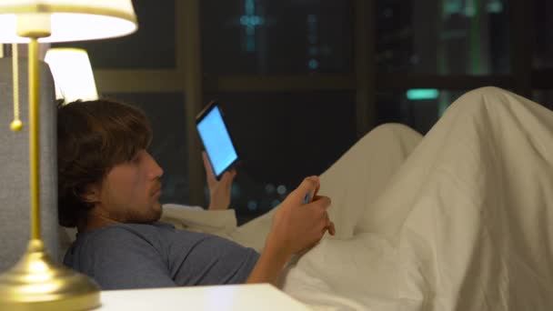 Mannen och kvinnan ligga i säng med smartphone och tablet pc. Man stänger av lampan och och går till vila medan kvinnan inte. problem i äktenskap och intersexual relationsproblem och mobil — Stockvideo