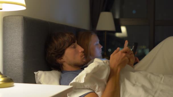 男と女横になっているベッドそれぞれスマート フォンとタブレット pc。結婚と菠薐草の人間関係の問題やモバイル デバイスの常習の概念の問題 — ストック動画