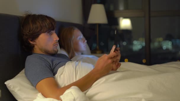 Uomo e donna sdraiati a letto ciascuno con smartphone e tablet pc. problemi nel matrimonio e nelle relazioni intersessuali problemi e concetto di dipendenza da dispositivi mobili — Video Stock