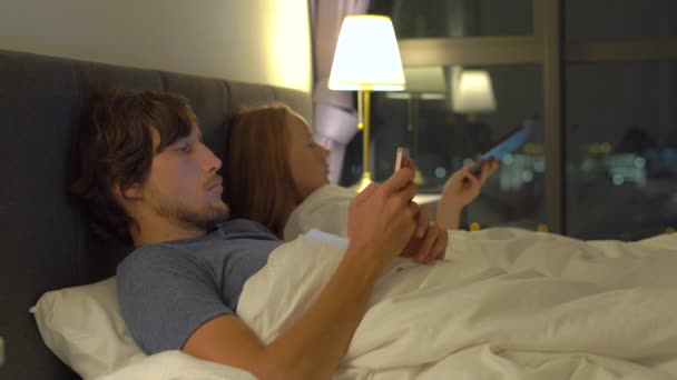 Mężczyzna i Kobieta, leżąc w łóżka każdego ze smartfona i tabletu. Kobieta wyłącza lampy i i idzie spać a człowiek nie. problemy w małżeństwie i problemy transseksualni relacji i komórkowego — Wideo stockowe