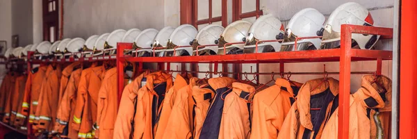 Close up of Fireman coats, helmets and boots wait for the next call. Dressing room of the volunteer fire department. BANNER long format