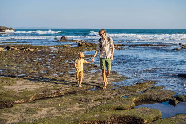 Father and son walking along cosmic Bali beach. Portrait travel tourists - dad with kid. Positive human emotions, active lifestyles. Happy young family on sea beach.