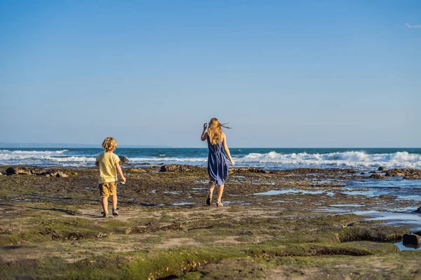 Mom and son walking along cosmic Bali beach. Portrait travel tourists - mom with kids. Positive human emotions, active lifestyles. Happy young family on sea beach.