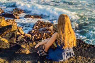 Anne ve oğlu kaya üzerinde oturan ve denizde seyir. Portre seyahat turistler - çocuk ile anne. Olumlu insan duyguları, aktif yaşam tarzları. Mutlu genç aile deniz plaj.