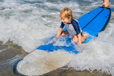 Mutlu bebek çocuk - genç sörfçü ile eğlenceli dalgalar deniz üzerinde sörf tahtası üzerinde binmek. Etkin aile yaşam tarzı, çocuklar açık su spor dersleri ve sörf kampı yüzme faaliyet. Çocukla tatil yaz.