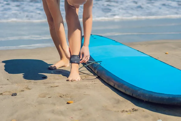 Young woman surfer getting on the surfboard's leash.